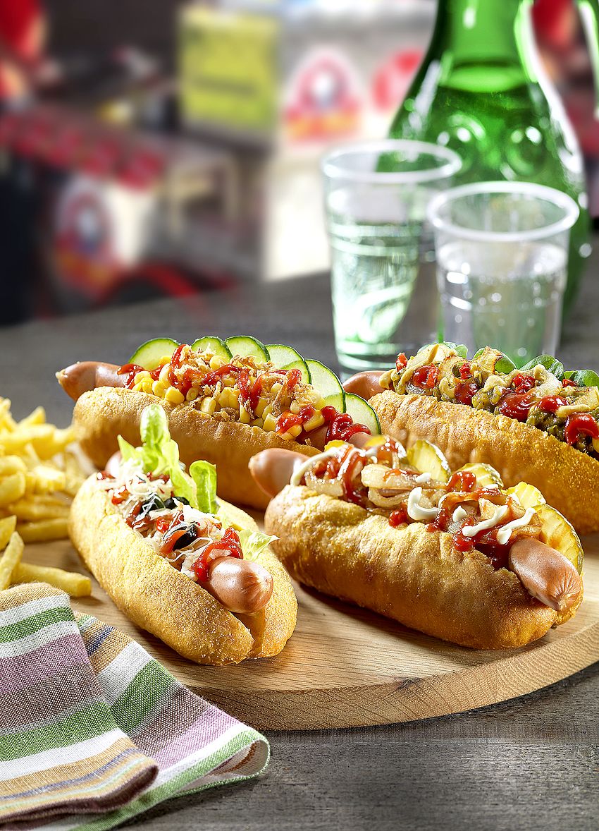 American Hot Dogs im Hot Dog Brötchen angerichtet mit Röstzwiebeln und Gurken auf Holzteller